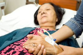 confined elderly woman holding a hand of her daughter